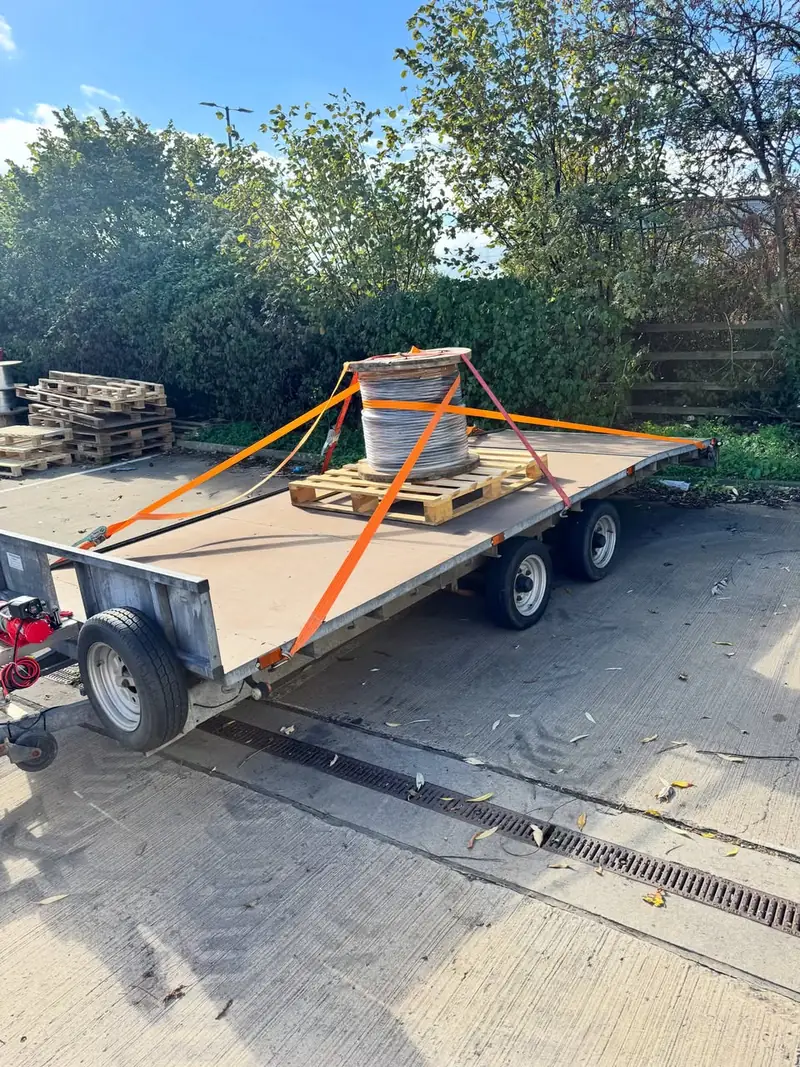 Flatbed trailer carrying a cable drum on a pallet, ratchet-strapped down