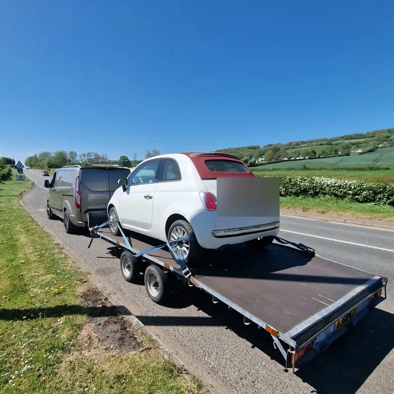 Fiat 500 being transported on a trailer along a country road